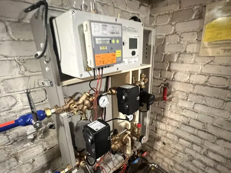 Fernwärme-Übergabestation mit Regler, Pumpen und Armaturen an einer Kellerwand